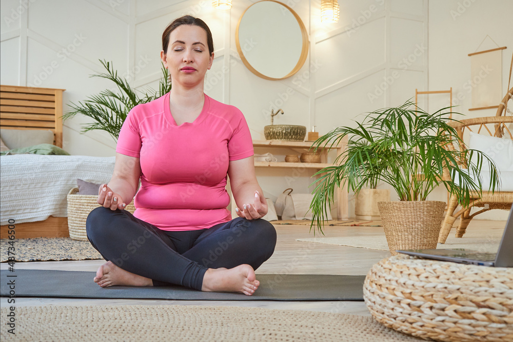 adult woman sits in a lotus position, meditates. Online training uses a laptop.