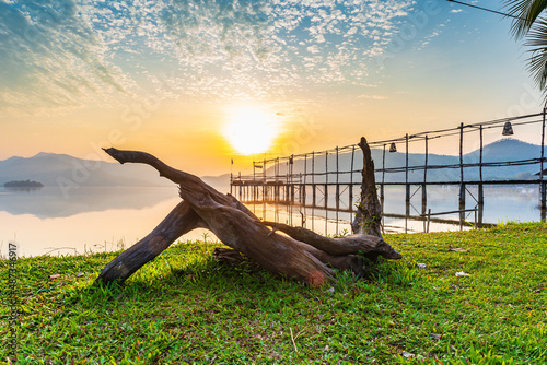 Landscape photo of Lake and mountain on the background in the morning time. and wooden bridge and old wooden tree root on the green grass lawn.