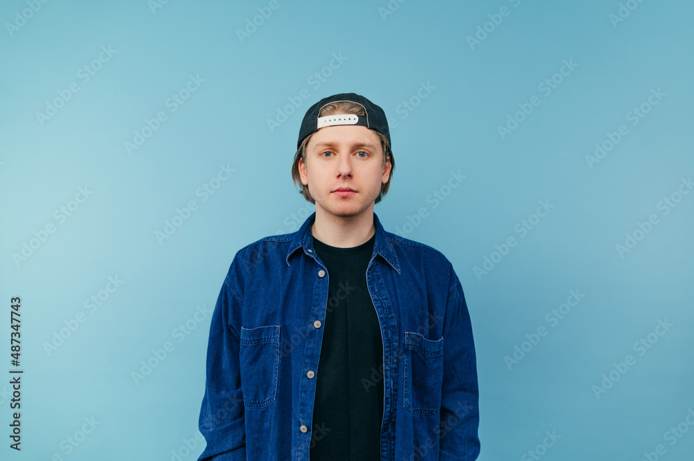 Handsome young man in denim shirt and cap isolated on blue background, looking at camera with serious face. Handsome young man in denim shirt and cap isolated on blue background, looking at camera with serious face.