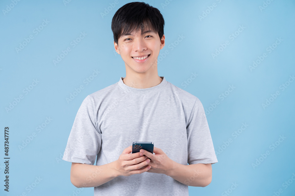 Young Asian man using smartphone on blue background Young Asian man using smartphone on blue background