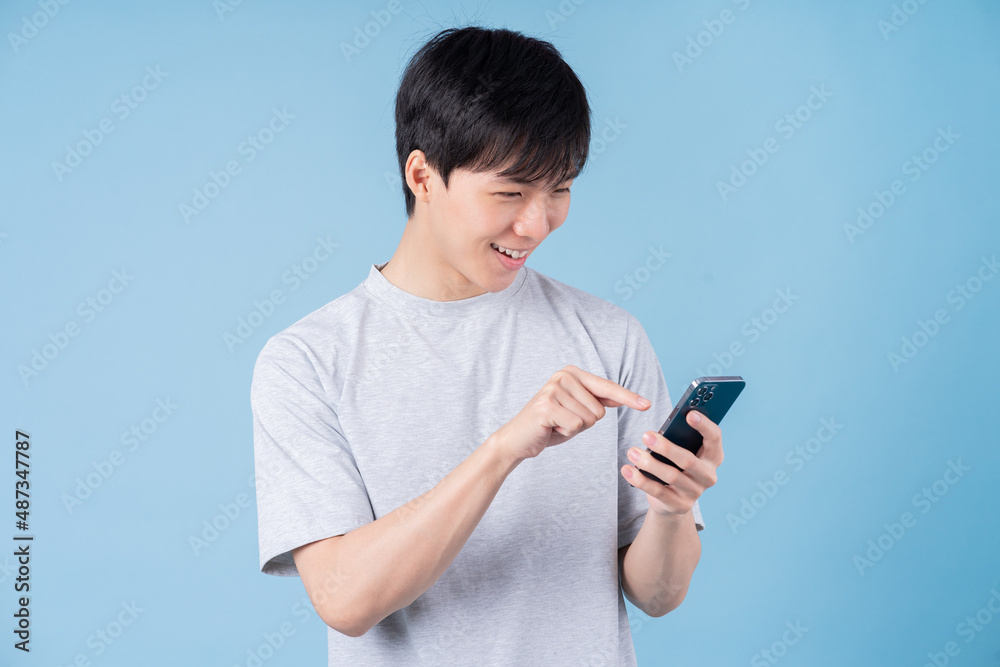 Young Asian man using smartphone on blue background Young Asian man using smartphone on blue background