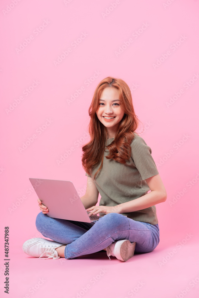 Naklejka premium Young Asian woman sitting and using laptop on pink background