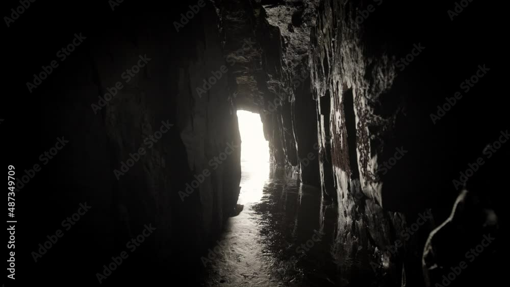 Dark cave by the ocean with light beaming through the end of the tunnel. Sand on the floor and its quiet and eerie with tide water.
