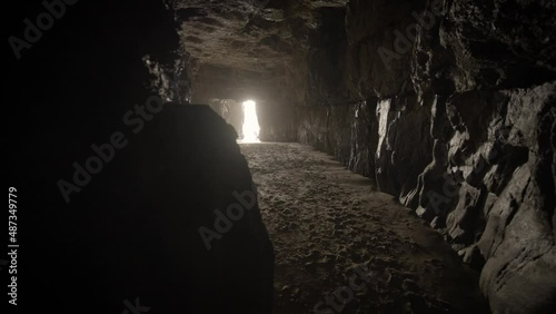 Dark cave by the ocean with light beaming through the end of the tunnel. Sand on the floor and its quiet and eerie. photo