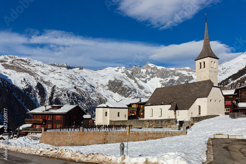 Winter view of small Swiss township of Bellwald with traditional wooden houses and parish church on background of rocky snow-capped Alps  photo