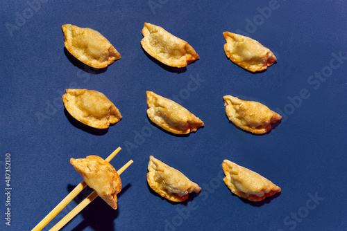 Pattern of fried gyoza dumplings, chopsticks holding one of them against a blue background photo