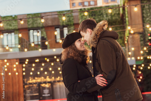 A young couple in love hug and smile against the background of a retro garland with light bulbs in winter