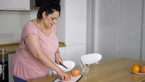 Attractive overweight woman preparing healthy meal, cutting grapefruit photo