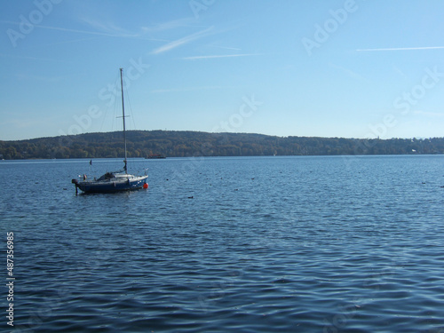 A sailboat on the Ammersee lake in Bavaria under clear blue and sunny sky with the forested shore in the background
