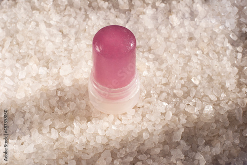 Crystal deodorant from alunite against the background of salt. Pink stick of eco deodorant on a white background of salt crystals. 
