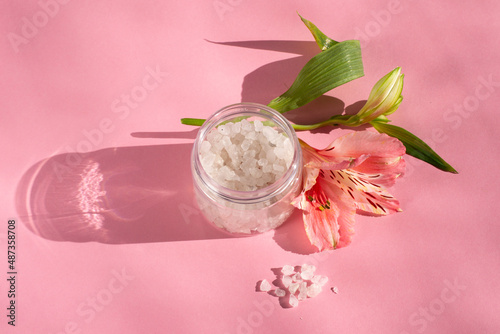 White bath salt with flowers on a pink background. Perfumed salt in a bottle. 