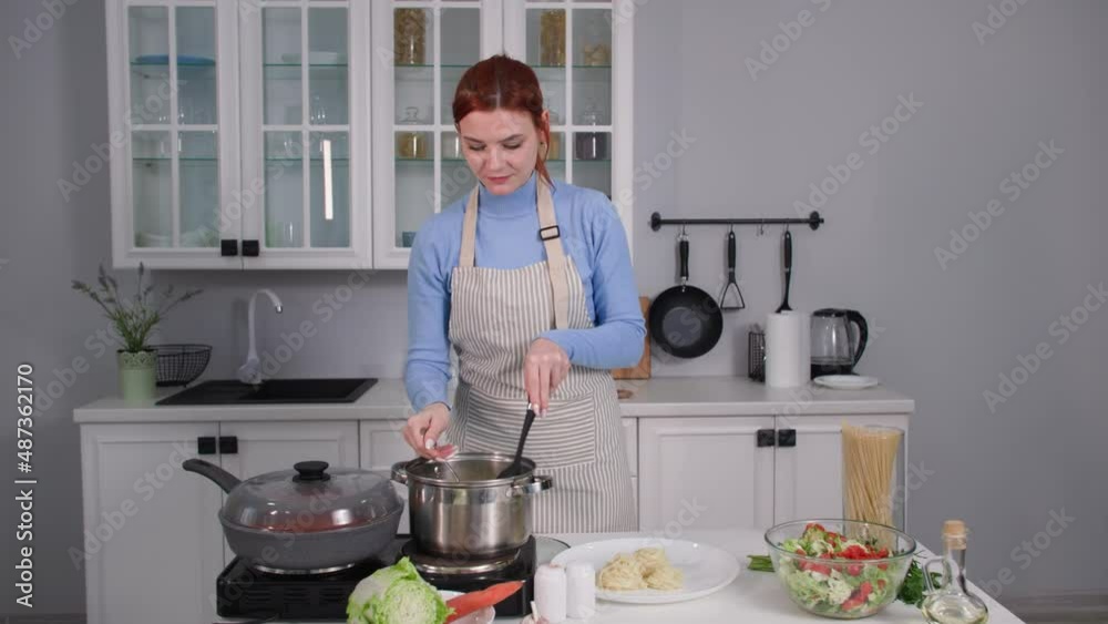 homemade food, a young housewife takes pasta out of the pan and puts it on her family's serving plate while standing in the kitchen. homemade food, a young housewife takes pasta out of the pan and puts it on her family's serving plate while standing in the kitchen.