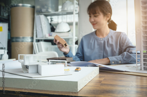 Modern house building model of architect women that was created as an example on the desk having material sample and blueprint in designer jobs.