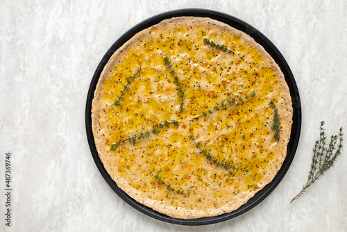 Unbaked focaccia round flat bread. Homemade pastry food with thyme herbs and salt top view.