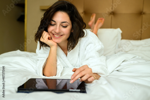 Beautiful woman wearing bathrobe and using digital tablet while lying on bed