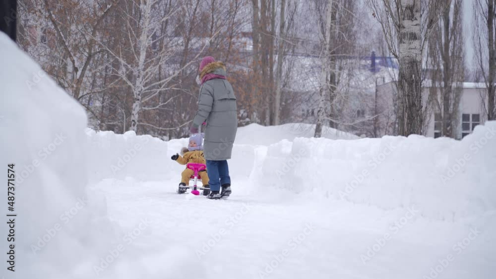 Mom runs and pulls a snowcat sled over the snow with a toddler sitting on it for 15-23 months in yellow warm clothes. Mom runs and pulls a snowcat sled over the snow with a toddler sitting on it for 15-23 months in yellow warm clothes.