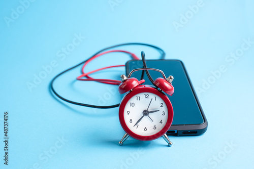 Mobile phone and clock connected with red and black wires, conceptual set as a external alarm clock. 