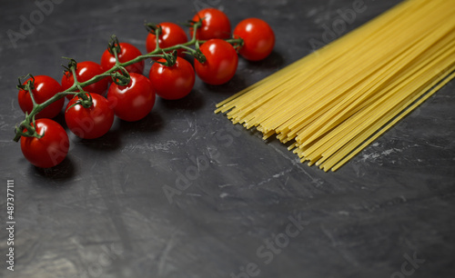 Cherry tomatoes branch and raw spaghetti - ingredients for making Italian pasta, on dark background, selective focus.