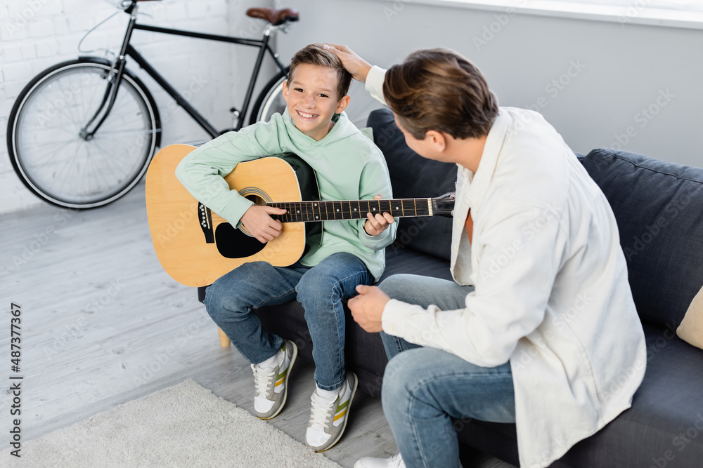 Man touching smiling son with acoustic guitar at home