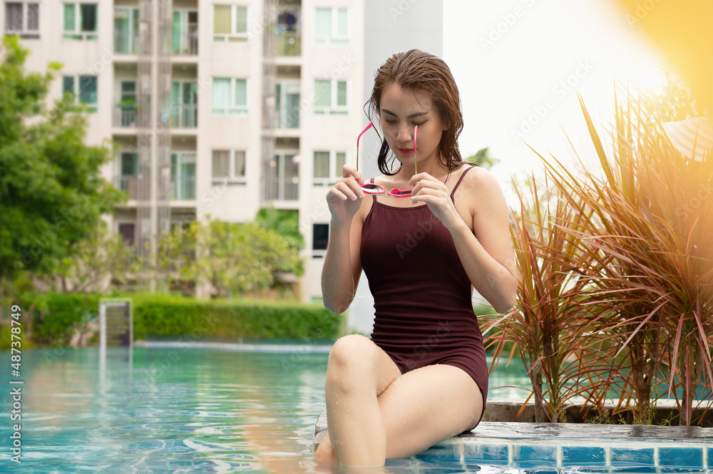 Asian beautiful young woman sitting and relaxing at the swimming pool with sunglasses. Travel spa resort pool, Relaxing place, Real estate.