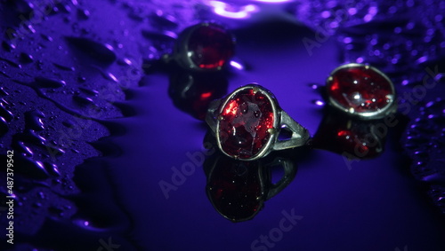 Vintage silver ring with a red stone against the background of silver earrings on a wet surface blue light abstraction selective focus