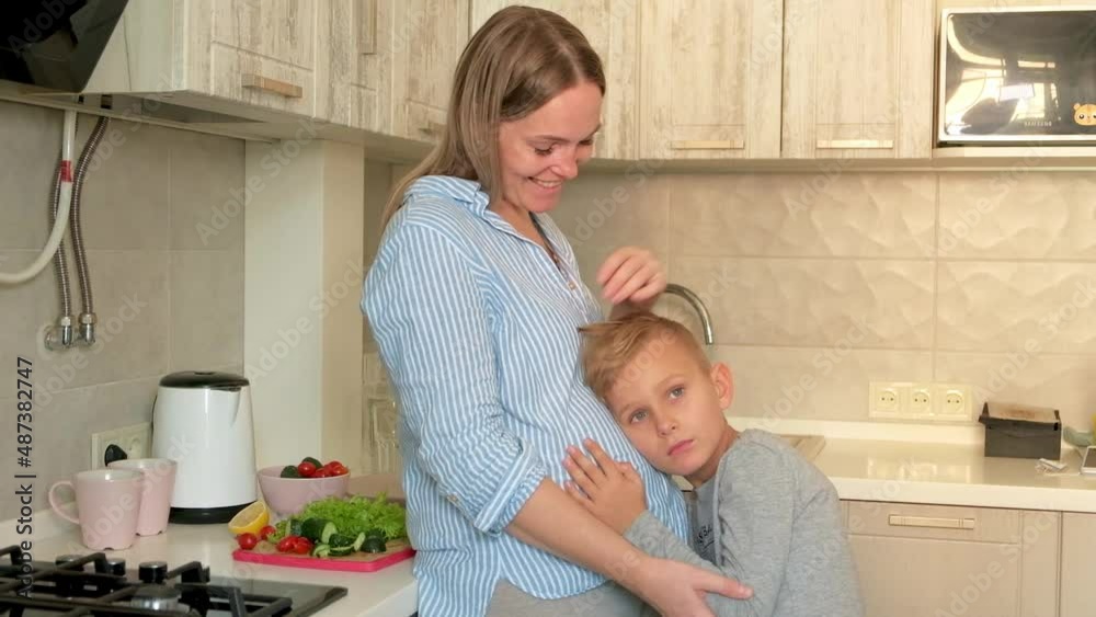 Pregnant mom with kid playing together and huging in the kitchen. Son listening to mom's pregnant belly Pregnant mom with kid playing together and huging in the kitchen. Son listening to mom's pregnant belly