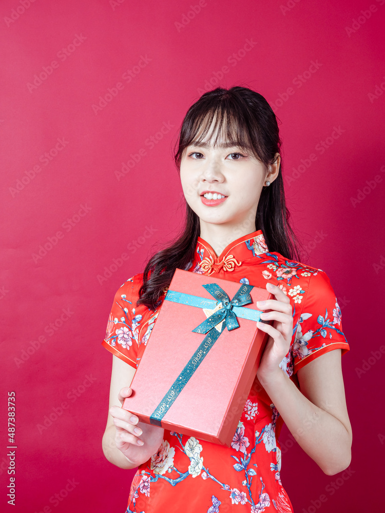 Portrait of a young asian woman wearing traditional cheongsam qipao dress holding gift isolated over red background. Portrait of a young asian woman wearing traditional cheongsam qipao dress holding gift isolated over red background.