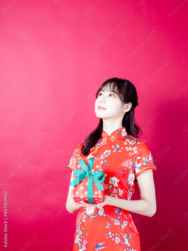 Portrait of a young asian woman wearing traditional cheongsam qipao dress holding gift isolated over red background. Portrait of a young asian woman wearing traditional cheongsam qipao dress holding gift isolated over red background.