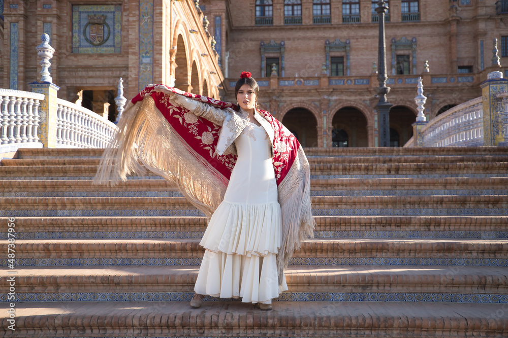 Young flamenco woman, Hispanic and brunette, in typical flamenco dance suit, dancing with red manila shawl with golden flowers, on stairs. Flamenco concept, dancer, typical Spanish dance.