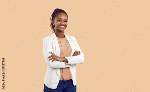 Studio portrait of happy successful confident black business woman. Beautiful young lady in white jacket smiling at camera standing isolated on blank solid beige colour copyspace background photo