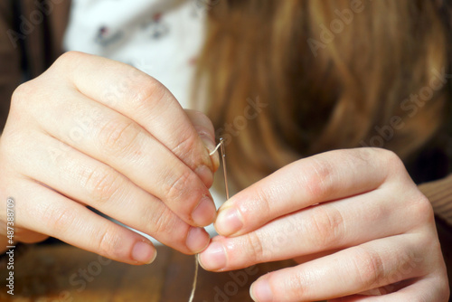 Women's hands threading the eye of a needle.