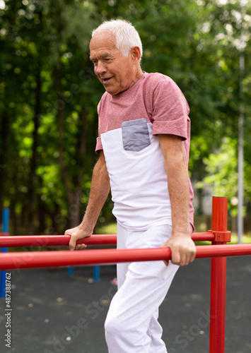 Senior man performing parallel bar exercises in park