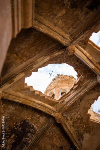 Photograph of the cross at the top of the church of Belchite through a hole caused by the bombs dropped in the Spanish civil war on a sunny day with a blue sky with some clouds