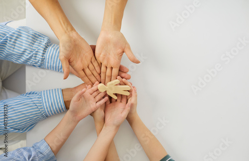 Happy young mum  dad and kids holding a little wooden toy figure of a child in their hands. Concept of family  adoption  love  care  protection  and safety. Top view close up  high angle closeup shot