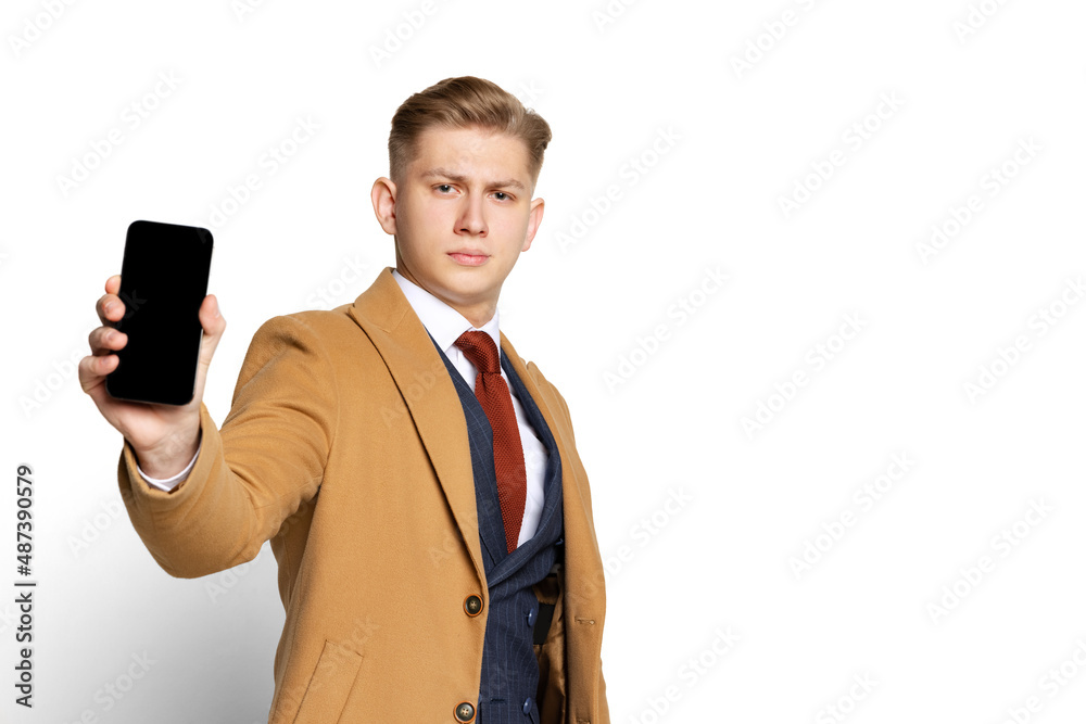 Portrait of young businessman, student, elegant man wearing suit and beige coat using phone isolated on white studio background. Portrait of young businessman, student, elegant man wearing suit and beige coat using phone isolated on white studio background.