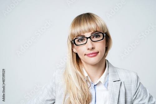 Obraz na płótnie Closeup portrait of happy young beautiful blonde woman in studio on light gray background. Smiling model in pantsuit and glasses. w salonie