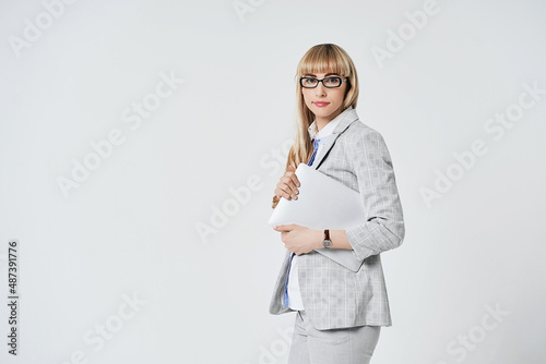 Obraz na płótnie Young beautiful blonde woman in studio on light gray background. Model in pantsuit and glasses with a silver laptop computer. w salonie