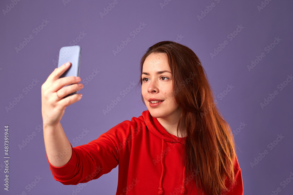 Close up portrait of caucasian woman in red clothes using her mobile on purple background Close up portrait of caucasian woman in red clothes using her mobile on purple background