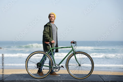 Young hispanic man waking with a bicycle at seaside.