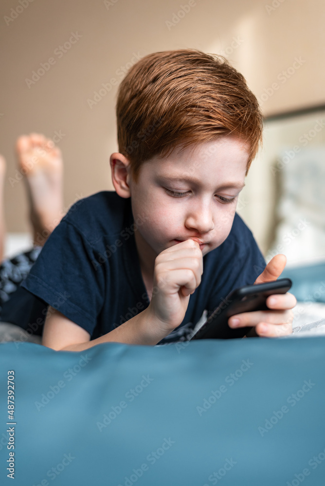Communication and technology concept - ginger boy thinking with smartphone, playing game at home or texting Communication and technology concept - ginger boy thinking with smartphone, playing game at home or texting