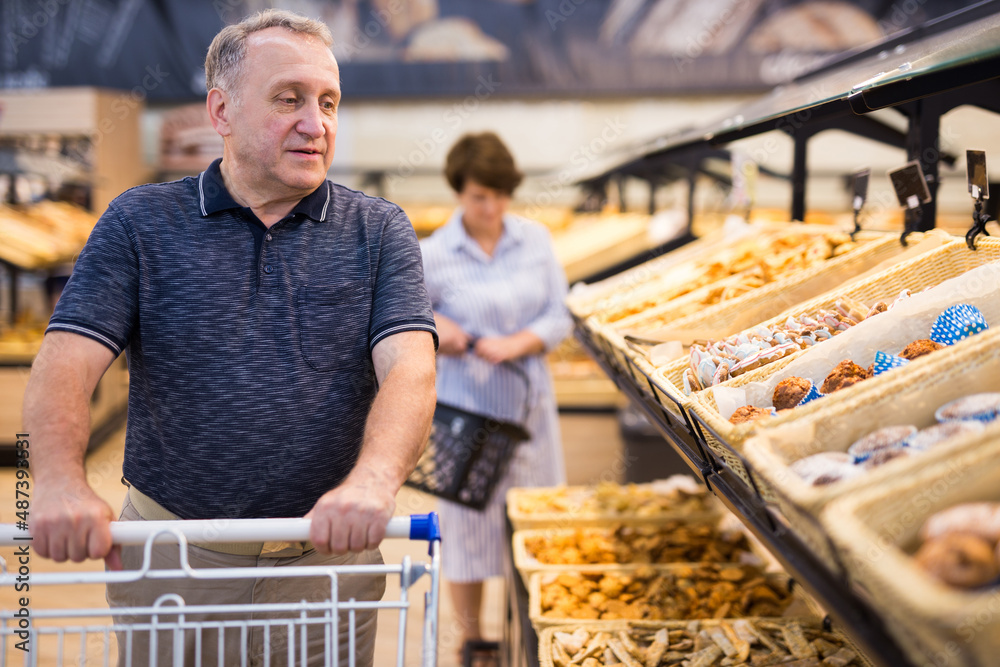 mature man choosing bread and baking in grocery section of supermarket