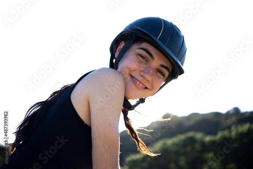 Portrait of a beautiful happy white woman smiling wearing a helmet while she is riding her horse with a forest in the background on a sunny day