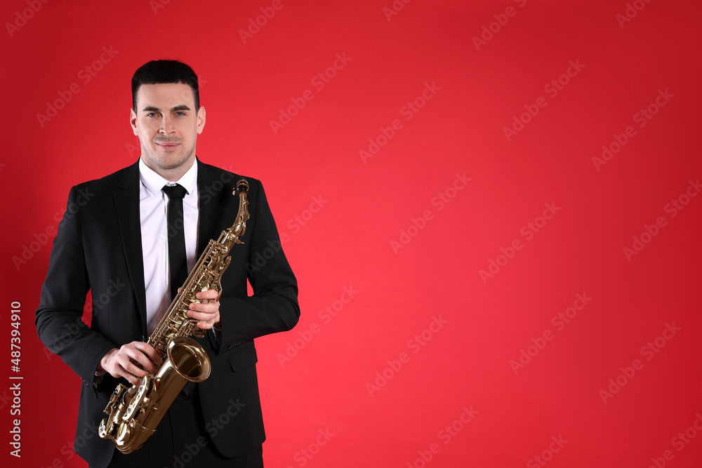 Fototapeta premium Young man in elegant suit with saxophone on red background. Space for text