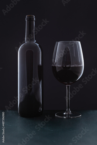 A red wine bottle without label and a full glass