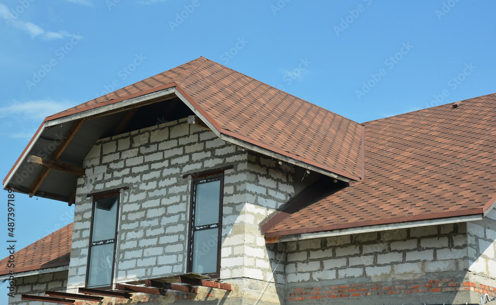 A close-up of an attic of one and a half storey house under construction with dormer windows, asphalt shingled roof, and the beginning of a loft balcony construction.Asphalt shingles roofing.