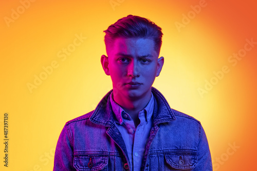 Closeup young handsome man wearing casual youth style clothes isolated on orange background in neon light, filter. Concept of emotions, beauty, fashion © master1305
