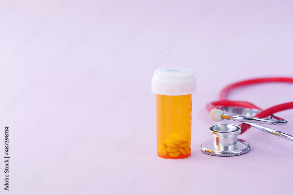 orange and white color pill container and stethoscope on color background 