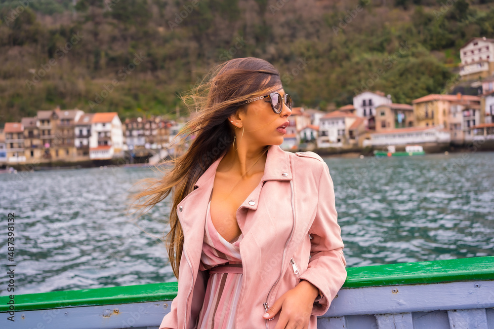 Pretty Latin woman with sunglasses sightseeing on a boat along the coast. Tourism in summer on vacation, mounted model looking at the horizon