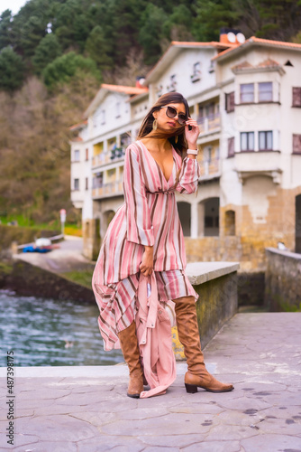 Portrait of a young Latin woman in a pink dress enjoying summer vacations in a beautiful coastal town, posing by the sea