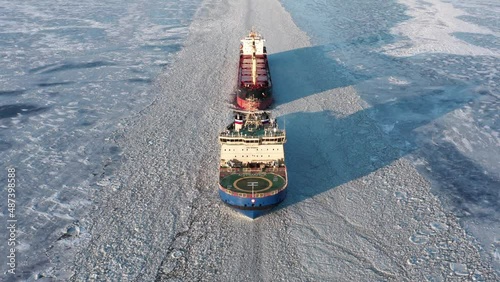 St. Petersburg, Russia, winter 2022: Icebreaker ship provide the way for cargo ship in north polar region. Sunny day. Drone view